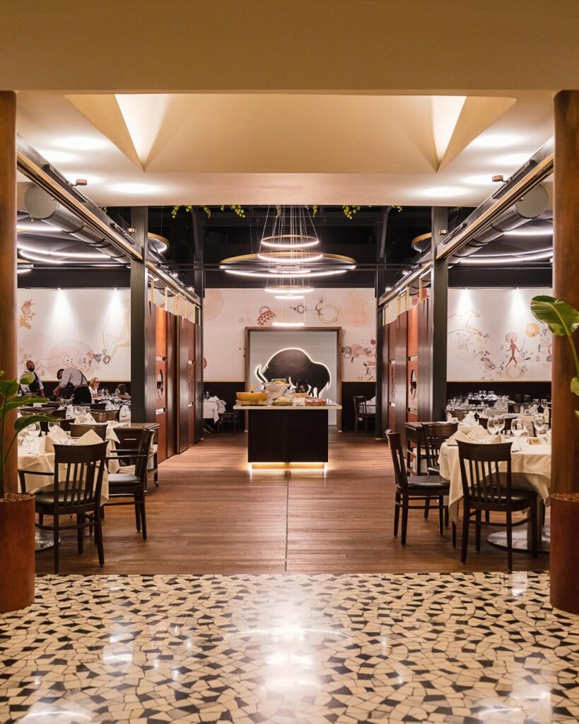 Interior view of Barbacoa Milano’s dining room with elegant wooden floors, white tablecloths, and ambient lighting.