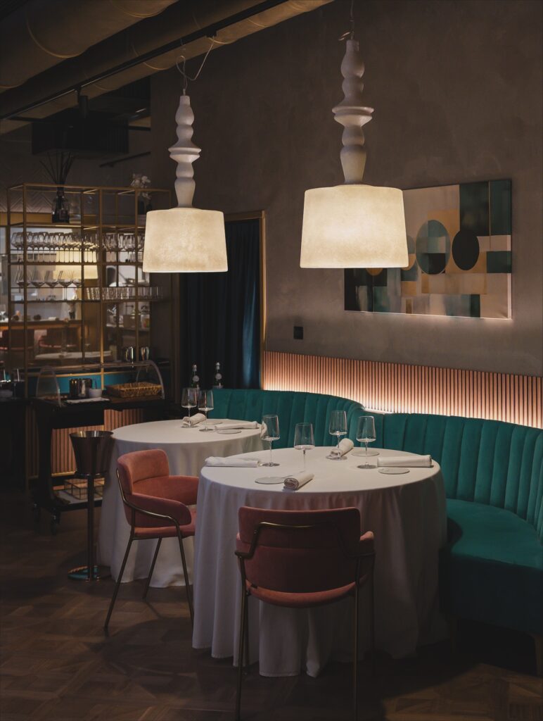 Interior of Procaccini Milano featuring round tables, teal banquette seating and warm modern lighting.
