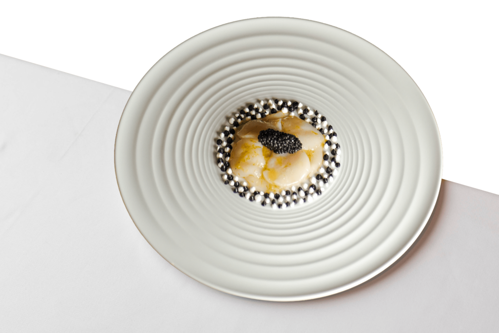 Close-up of a gourmet scallop dish topped with caviar at Procaccini Milano, presented on a textured white plate.