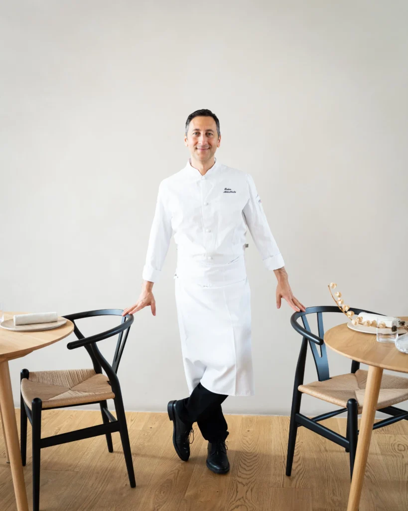 Portrait of chef Fabio Abbattista of Abba Milano standing between dining tables in a minimalist restaurant interior.