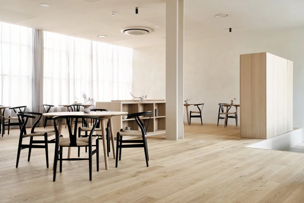 Interior of Abba Milano with wooden floors, round tables, black chairs and soft natural lighting.