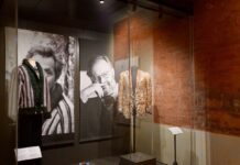 The Gentleman in Milan: A Free Fashion Exhibition Display case at Palazzo Morando’s “The Gentleman” exhibition in Milan with two menswear jackets, men’s jewelry on pedestals, and large black-and-white portrait backdrops.