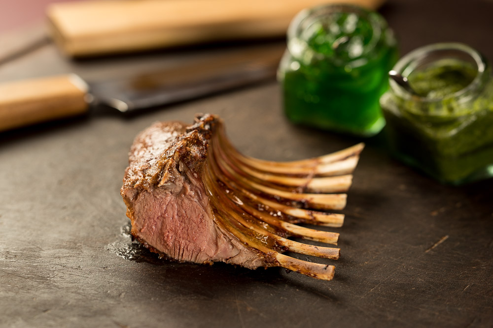 Valentine’s Day in Milan: Where to Find a World-Class Steakhouse Experience with a Brazilian Twist Close-up of a large skewer of grilled lamb chops being carved with a knife, showing the juicy interior of the meat.