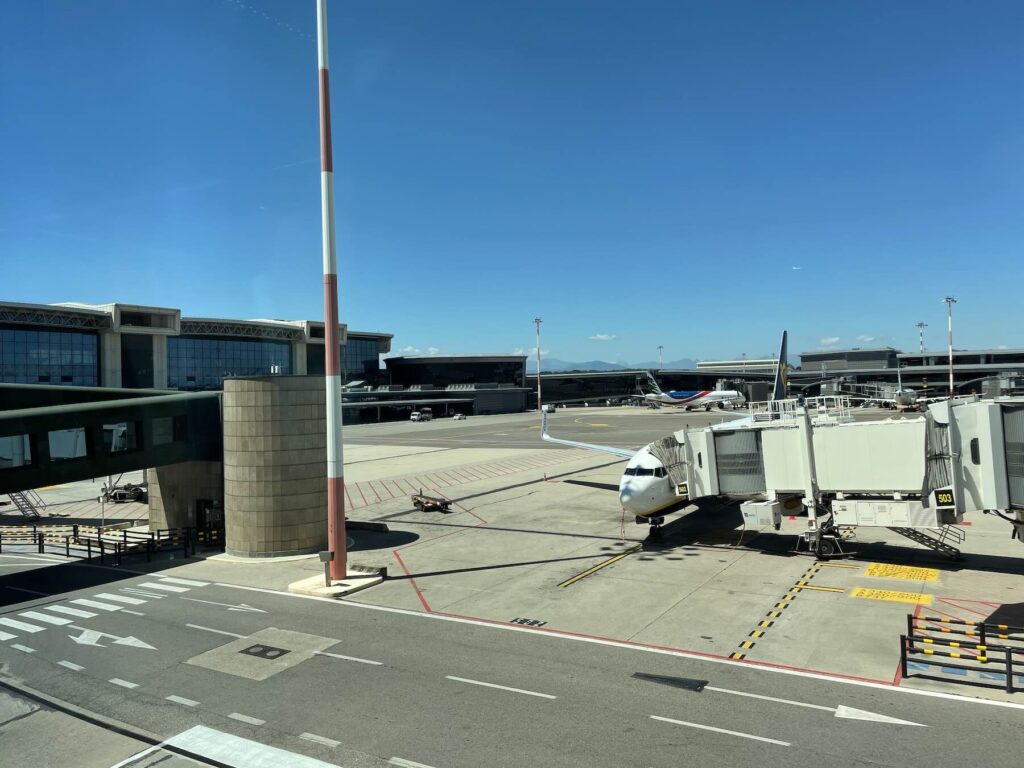 Milan Malpensa Airport Runway Closure: What Travelers Need to Know (March-May 2026) - In the photo: Aircraft parking apron at Milan Malpensa Airport showing commercial airplane connected to terminal via jet bridge, blue sky in background