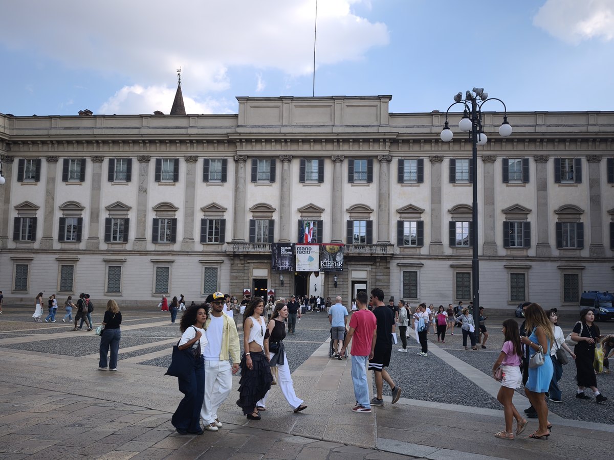 Facade of Palazzo Reale on Piazza del Duomo in Milan, with people walking past exhibition banners